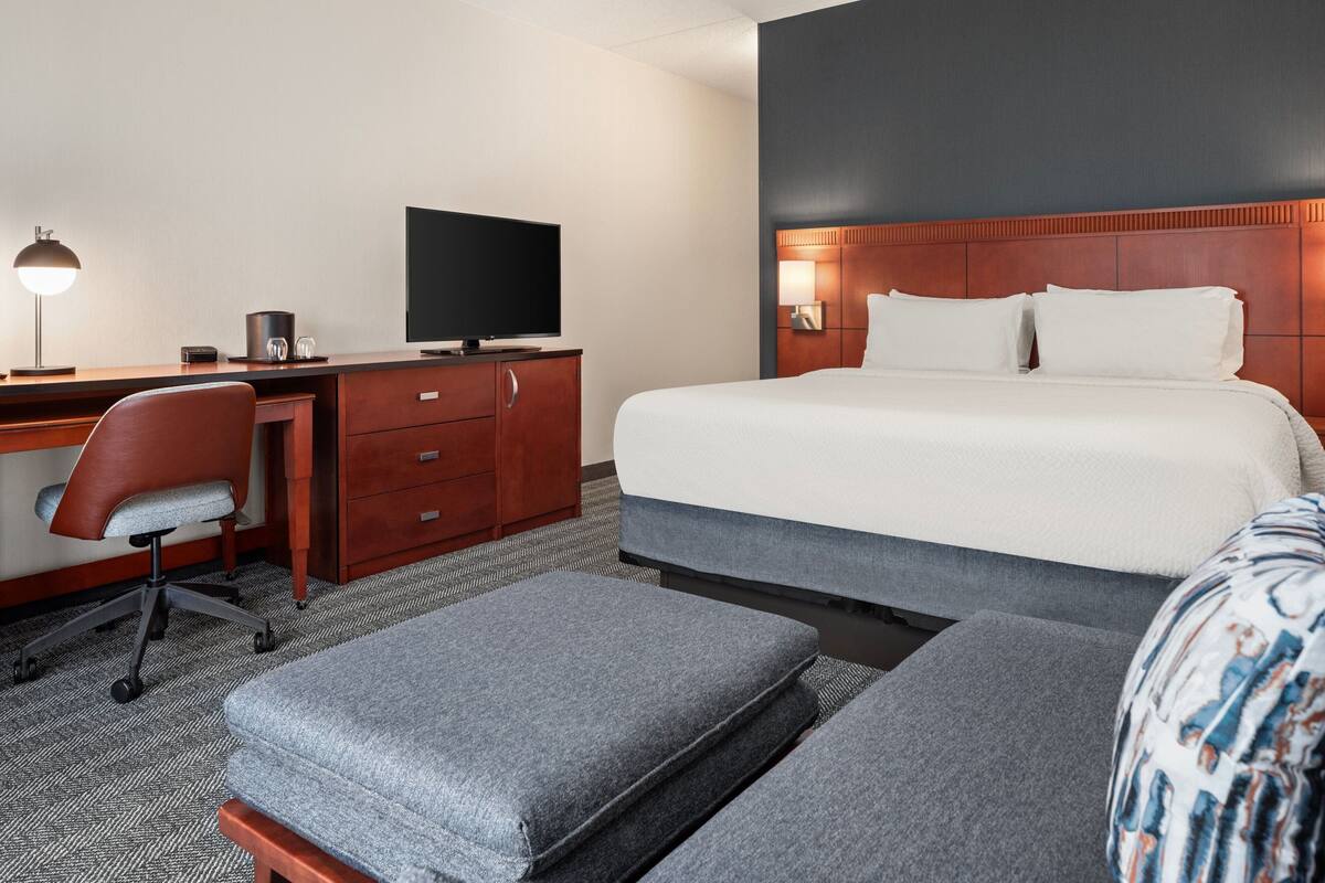 A hotel room with a bed, a desk with a computer, a chair, and a TV.