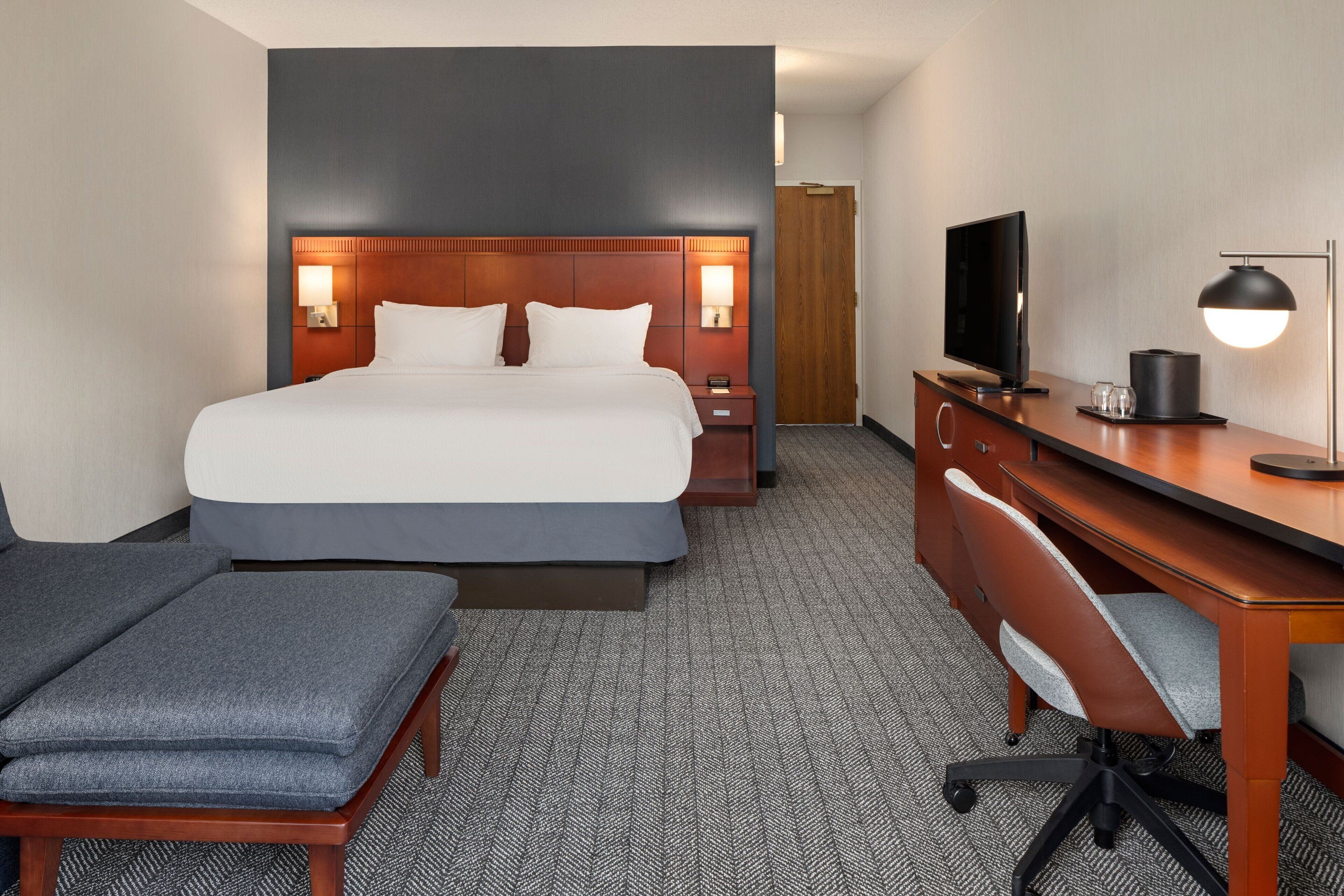 A hotel room with a large bed, a desk with a computer, a TV, and a lamp.