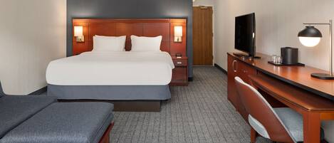 A hotel room with a large bed, a desk with a computer, a TV, and a lamp.