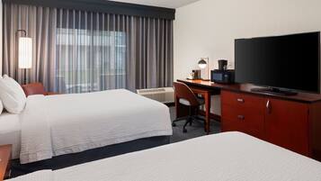 A hotel room with two beds, a desk with a TV, a lamp, and a coffee maker.
