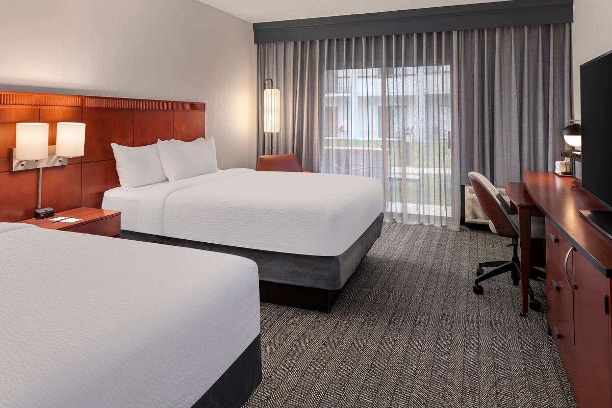 A hotel room with two beds, a desk, and a TV.