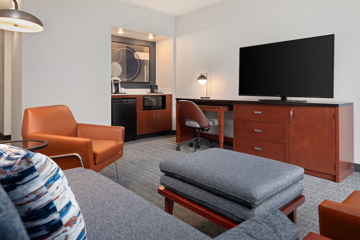 A hotel room with a sofa, a desk, a television, a chair, and a kitchenette.