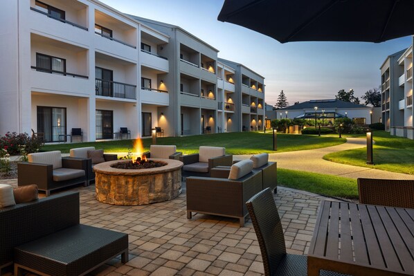 An outdoor patio area with a fire pit, seating, and a view of a multi-story building. - Courtyard Chicago Waukegan Gurnee (Waukegan)