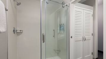 A glass-enclosed shower with a handheld showerhead, a white towel, and a white door with louvered panels.