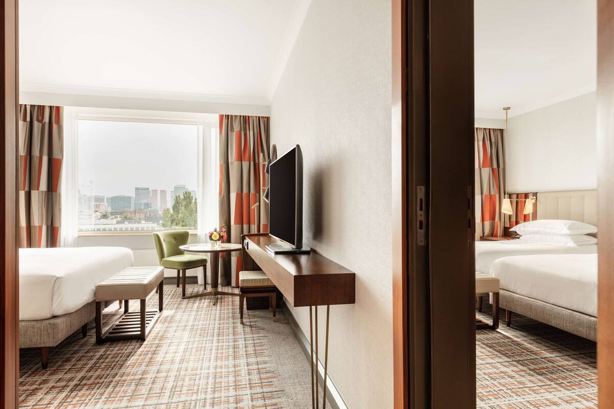 Habitación de hotel con dos camas, un escritorio, un televisor y vistas a la ciudad.
