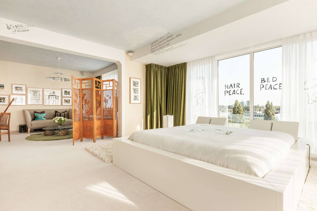 Un dormitorio moderno con una cama grande, un sofá y vistas de la ciudad a través de amplios ventanales.