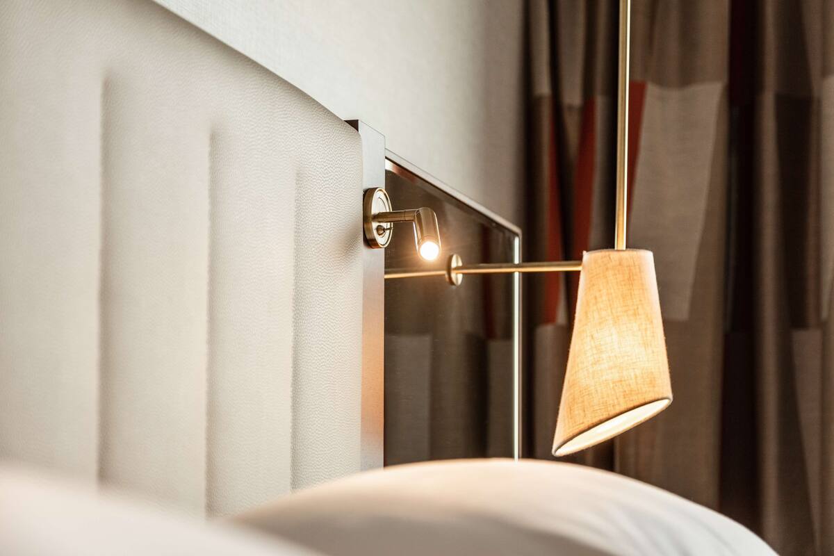 Habitación moderna con lámpara de pared, un espejo y vista parcial de una cama.