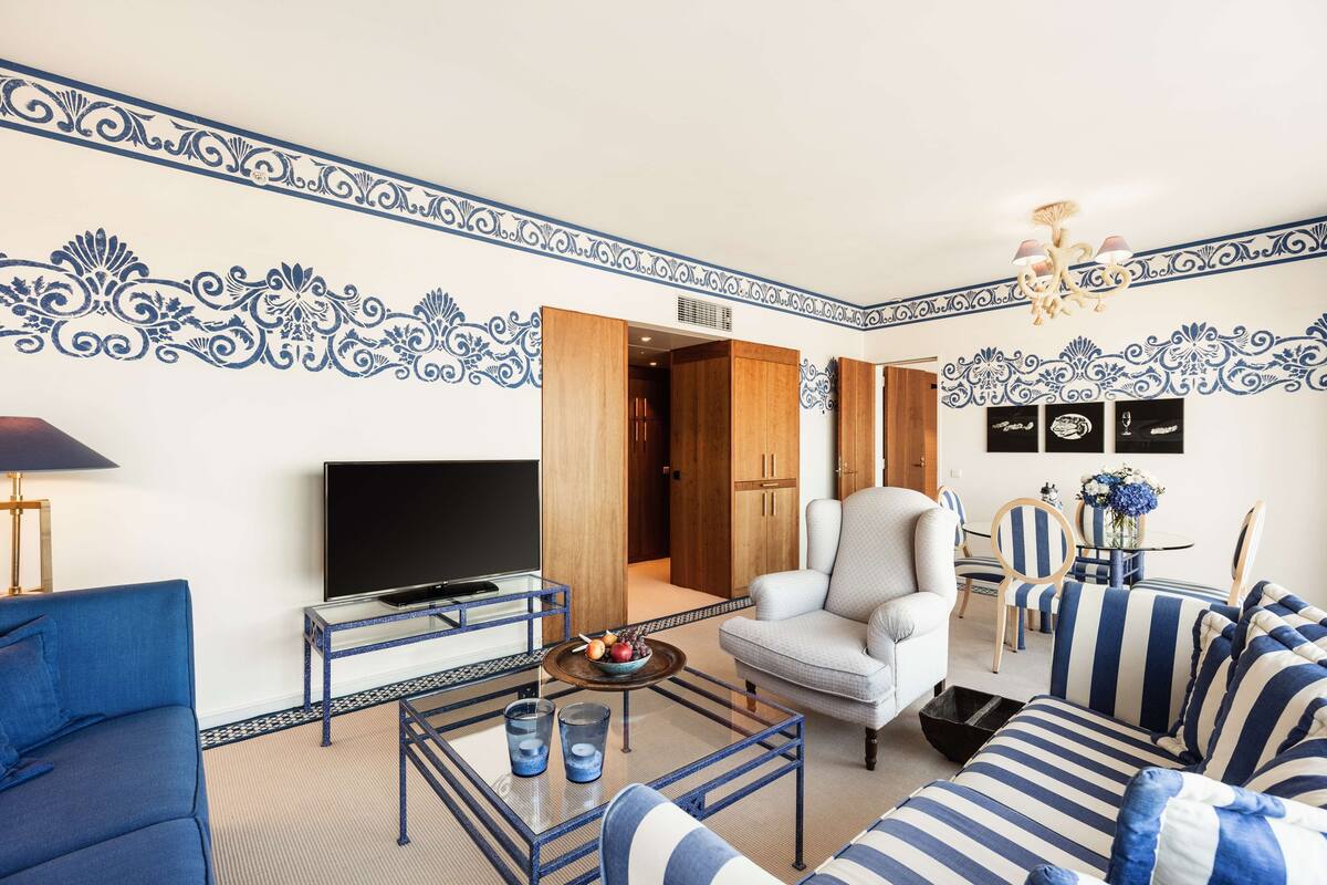 Una sala de estar con televisor, sofá, sillón y un comedor con sillas y mesa.