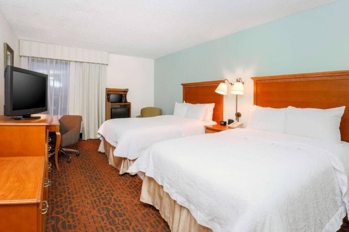Una habitació d'hotel amb dos llits, una taula de treball amb televisió, una cadira, una làmpada i una taula petita.