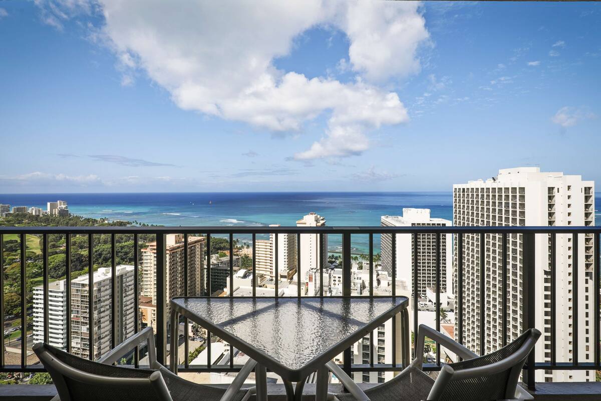 A balcony with a table and chairs overlooking a cityscape and ocean.