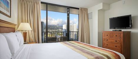 A hotel room with a large bed, a television, a dresser, and a balcony with a city view.