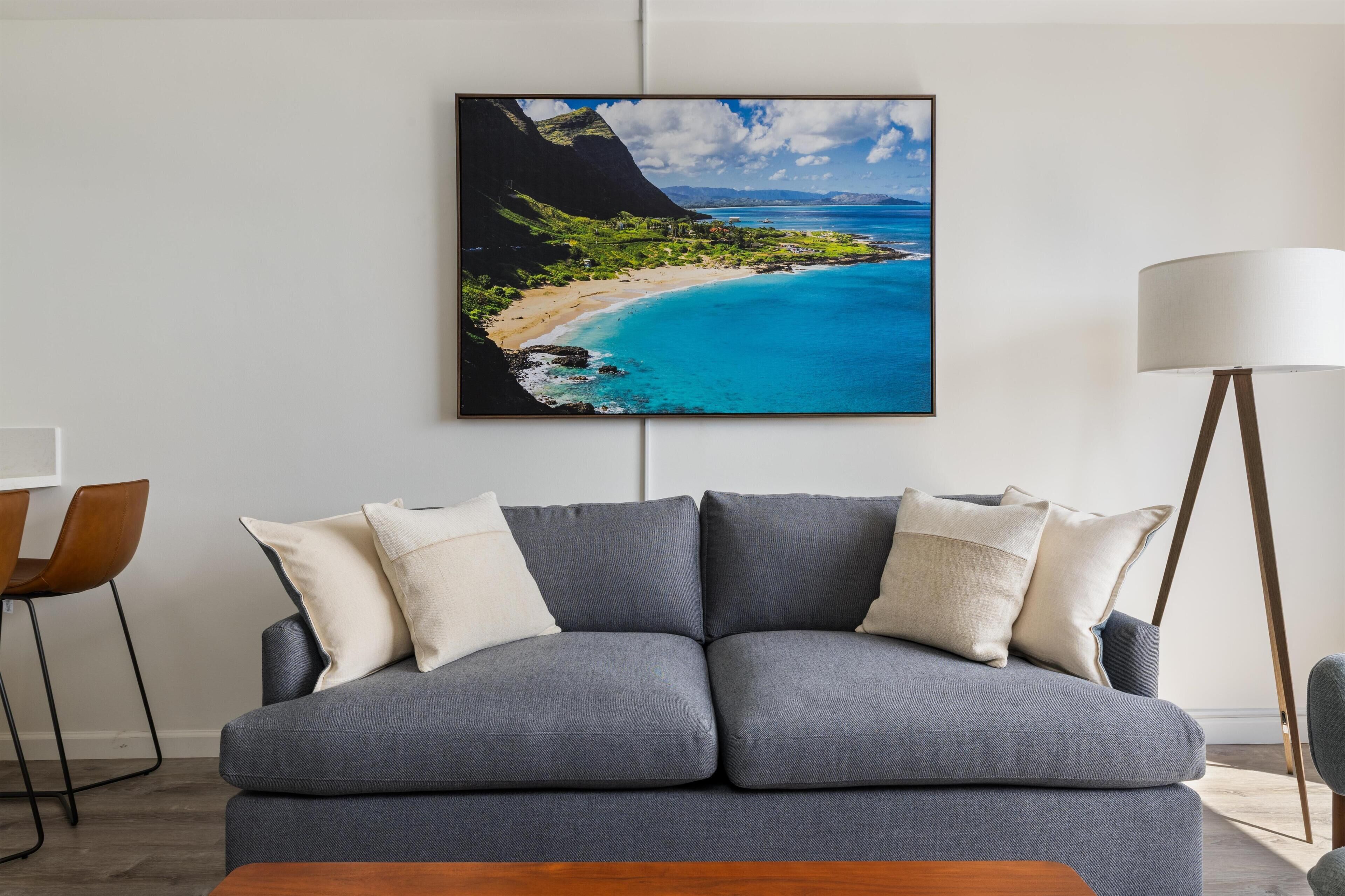 A modern living room with a grey sofa, a coffee table, and a framed landscape painting of a beach.