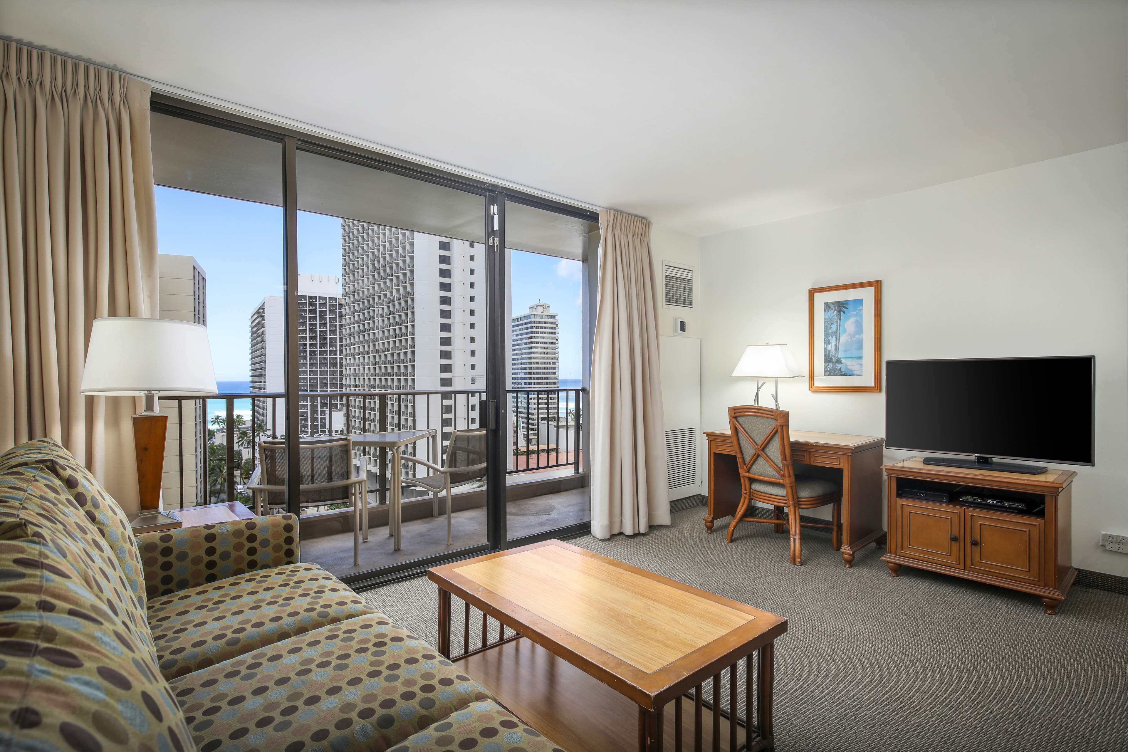 Une chambre d’hôtel avec un balcon, un canapé, une télévision, un bureau et une chaise.