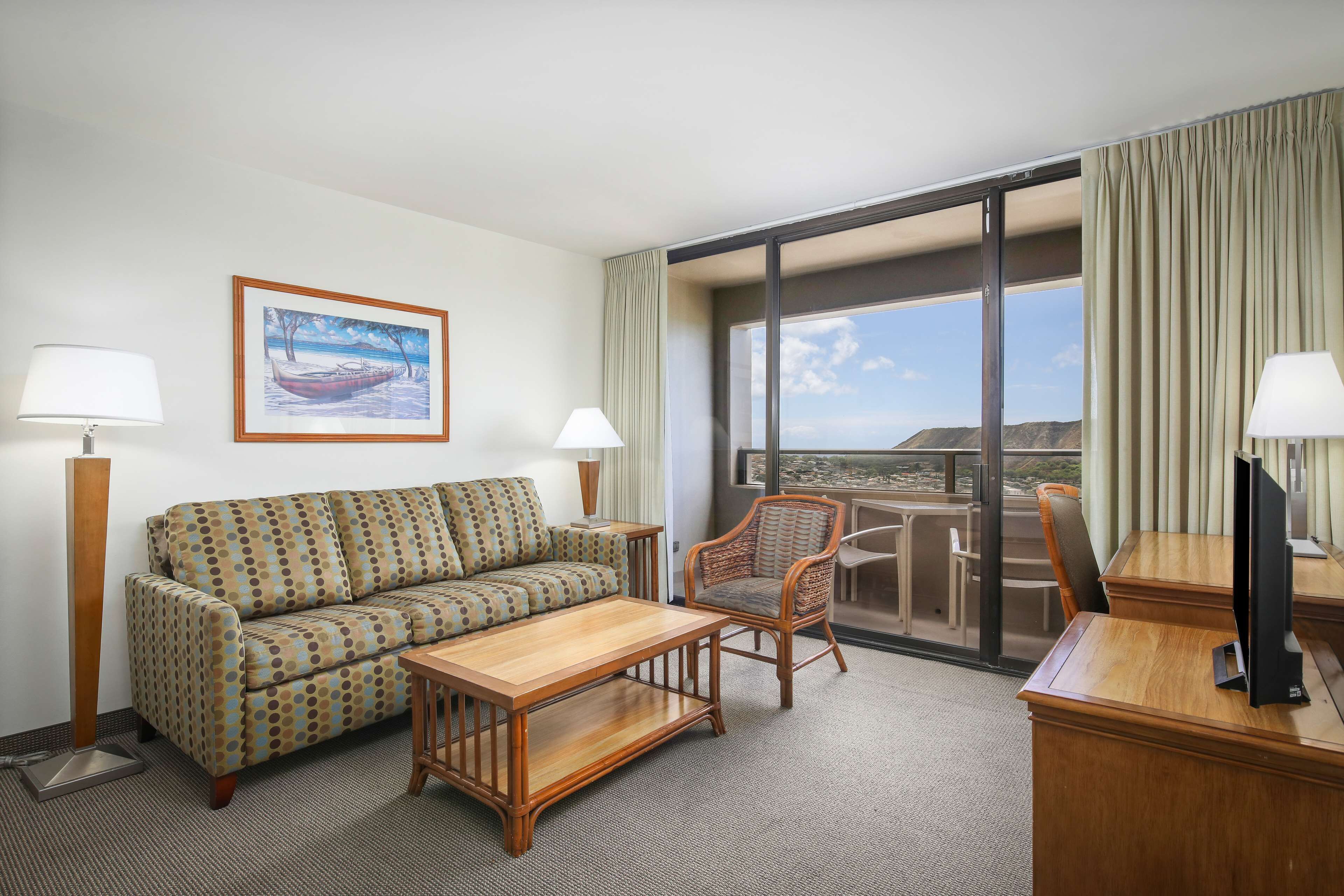 Habitación de hotel con sofá, sillón, mesa de comedor, televisor y un ventanal con vistas a las montañas.