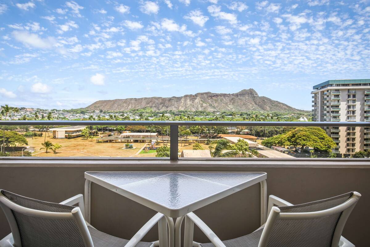 A balcony with a table and chairs, overlooking a town with a prominent mountain in the background.