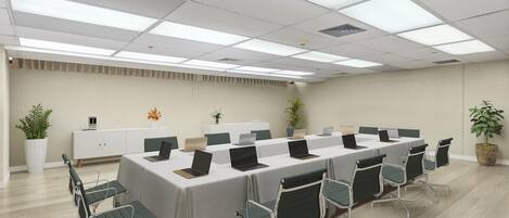 Un salón de conferencias con una larga mesa, varias sillas y un techo blanco con iluminación fluorescente.