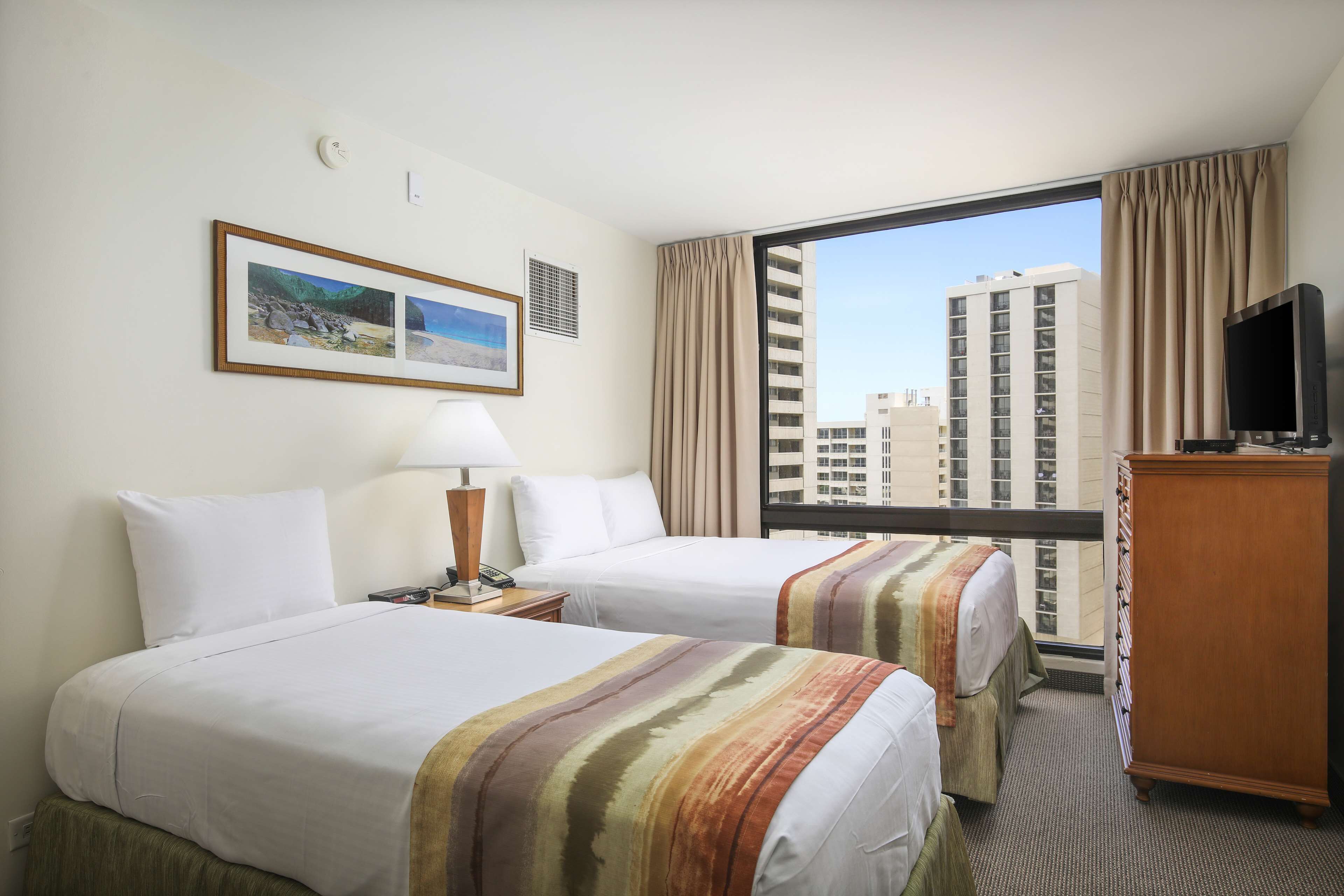 A hotel room with two beds, a TV, a dresser, and a large window with a city view.
