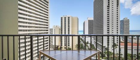 A balcony with a table and chairs, overlooking a cityscape with tall buildings and a clear sky.