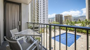 A balcony with a table and chairs, overlooking a swimming pool and a cityscape. - Aston Waikiki Sunset (Honolulu)