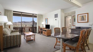 A hotel room with a large sliding glass door to a balcony, a dining area with a table and chairs, a sofa, a TV, and a kitchenette. - Aston Waikiki Sunset (Honolulu)