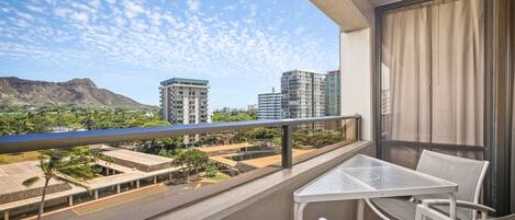 Un balcon avec une table et des chaises, donnant sur un parking et des immeubles.