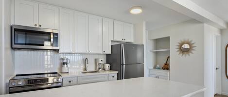 A modern kitchen with white cabinetry, a stainless steel refrigerator, a microwave, and a stove.