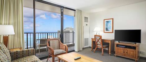 A hotel room with a balcony, a sofa, a table, a TV, and a chair.