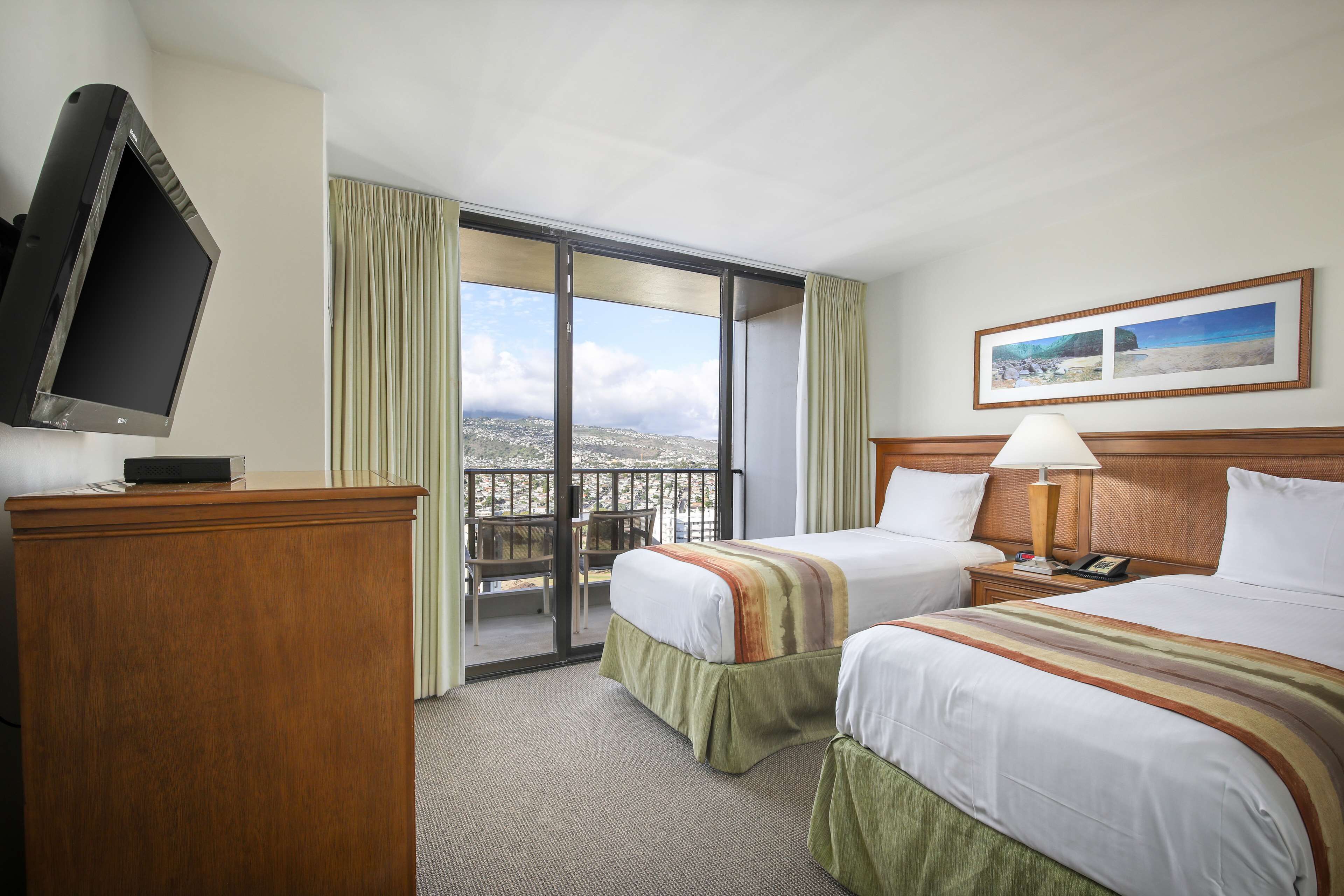 A hotel room with two beds, a TV, a balcony with a view, and a painting on the wall.