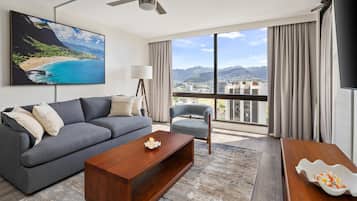 A modern hotel room with a large window, a sofa, a coffee table, and a painting of a beach scene.