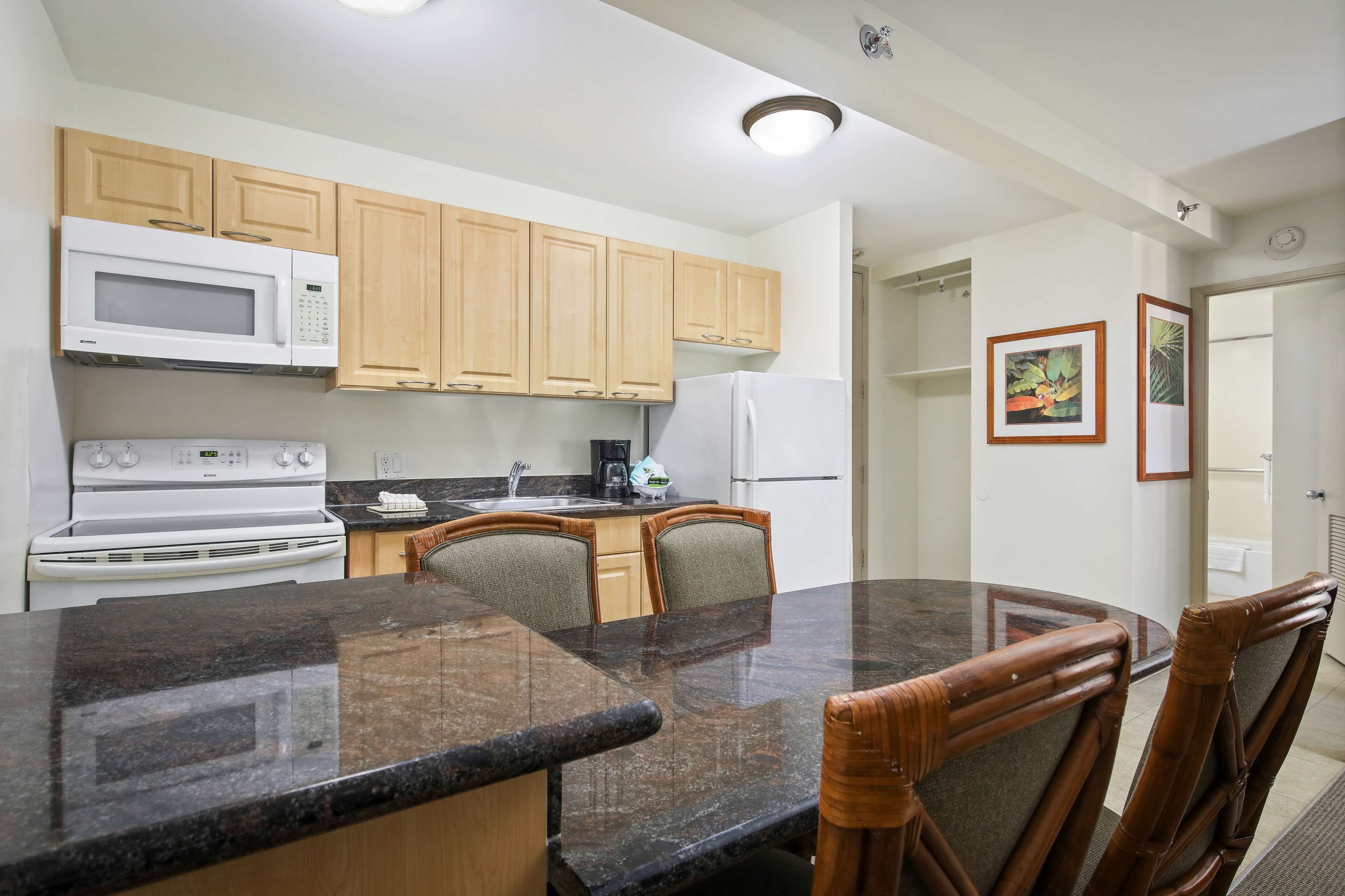 A kitchen with wooden cabinets, a microwave, stove, and a dining area with a granite countertop and wooden chairs.