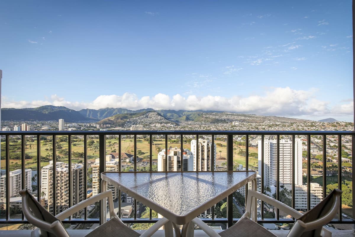 A balcony with a view of a cityscape, including high-rise buildings and mountains.