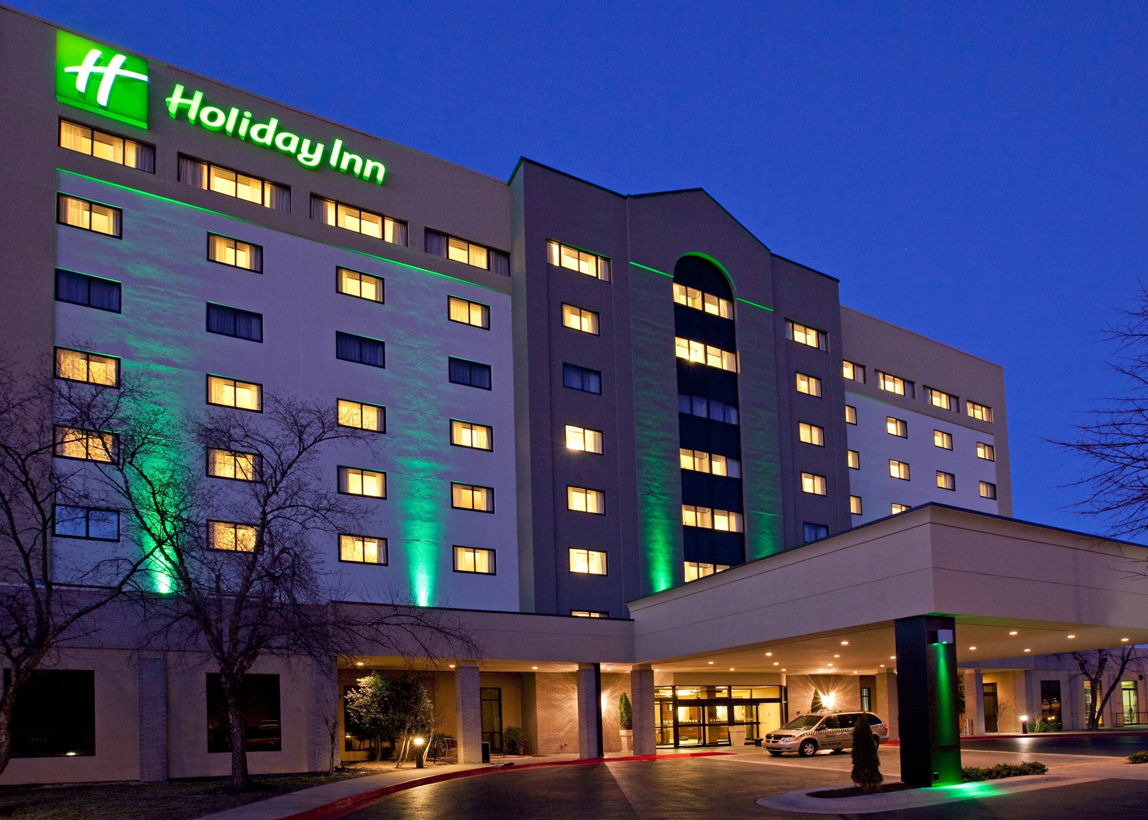 A Holiday Inn hotel with multiple floors, a well-lit entrance, and a parking area.