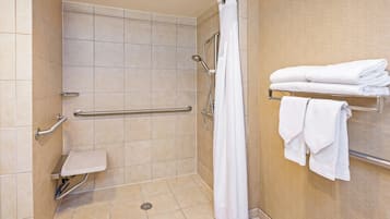 A shower area with a grab bar, a white shower curtain, and a towel rack with folded towels.