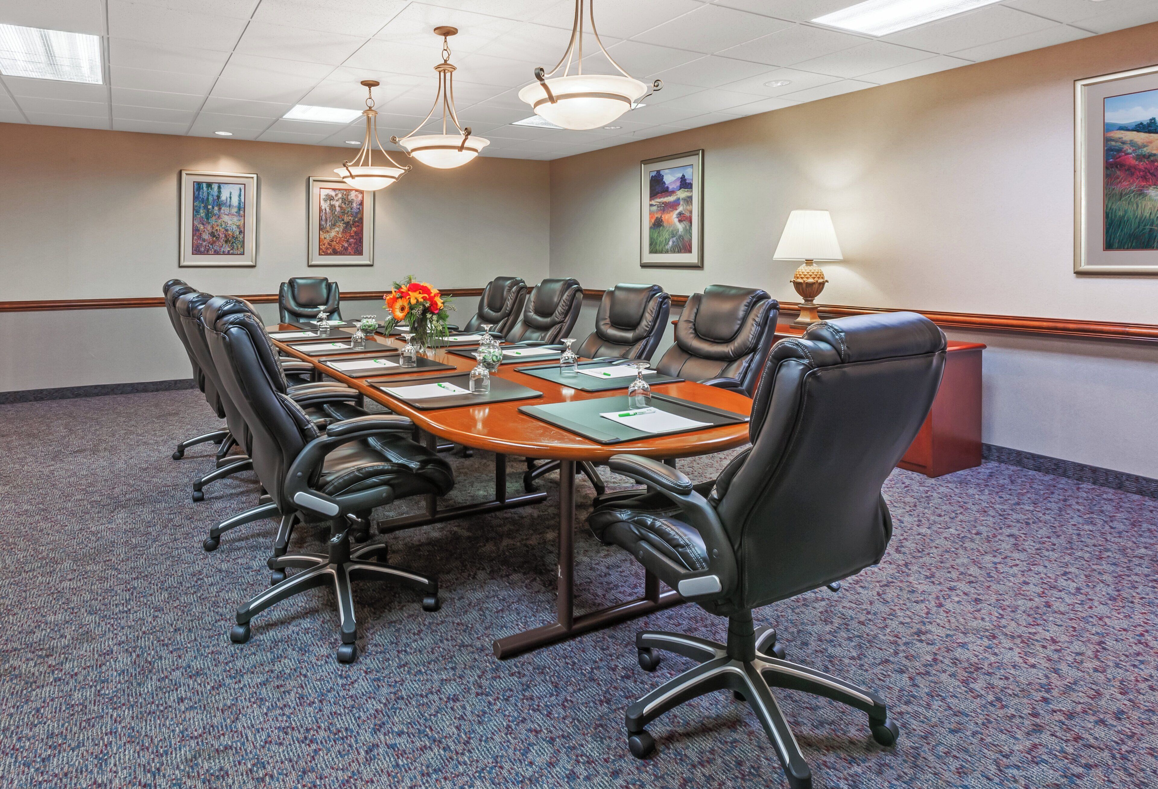A conference room with a long table, black leather chairs, and framed artwork on the walls.