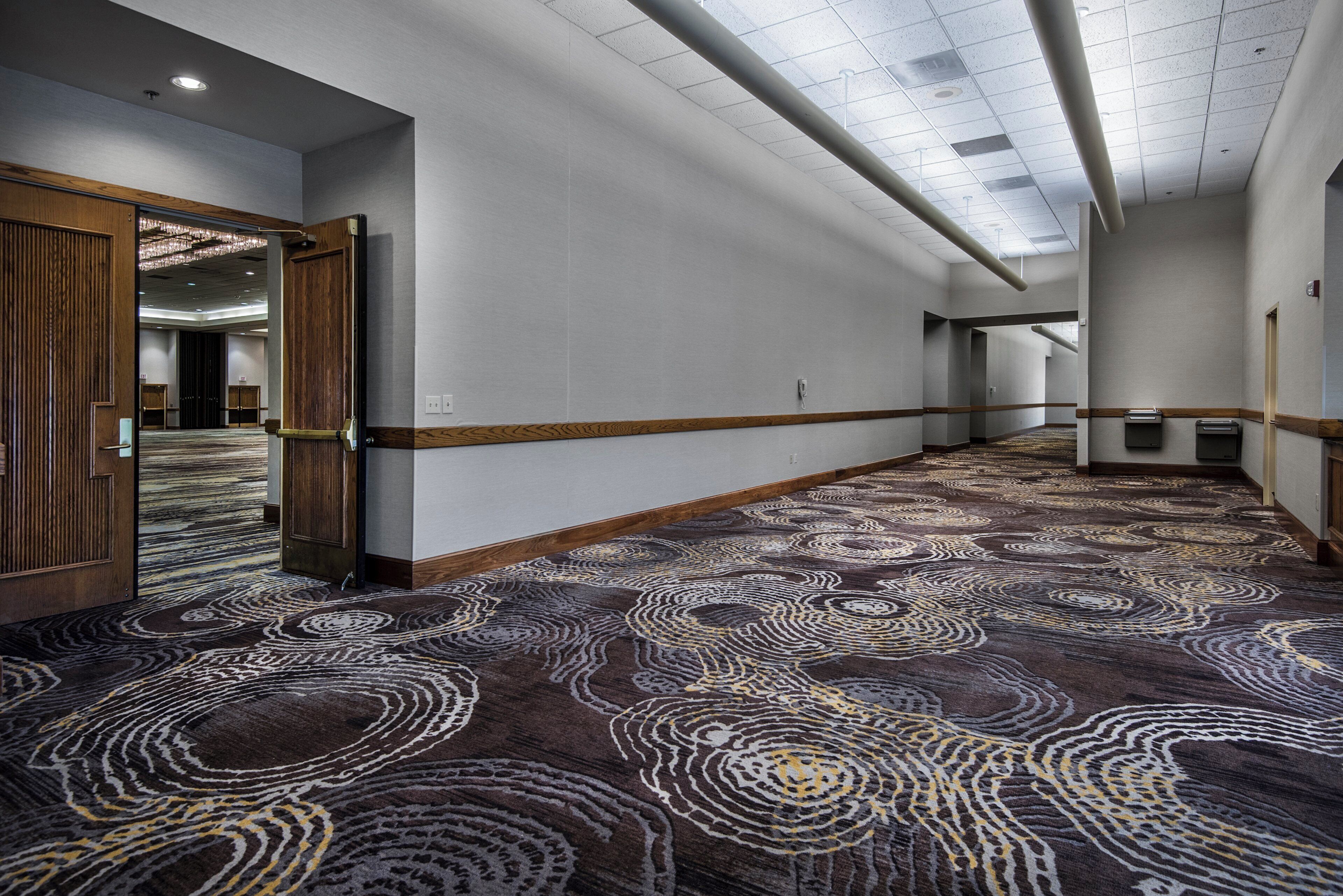 Un pasillo de hotel con alfombra estampada, marcos de puerta de madera e iluminación empotrada en el techo.