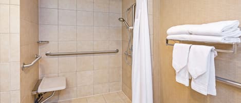 A shower with a grab bar, a white shower curtain, and a towel rack with folded towels.