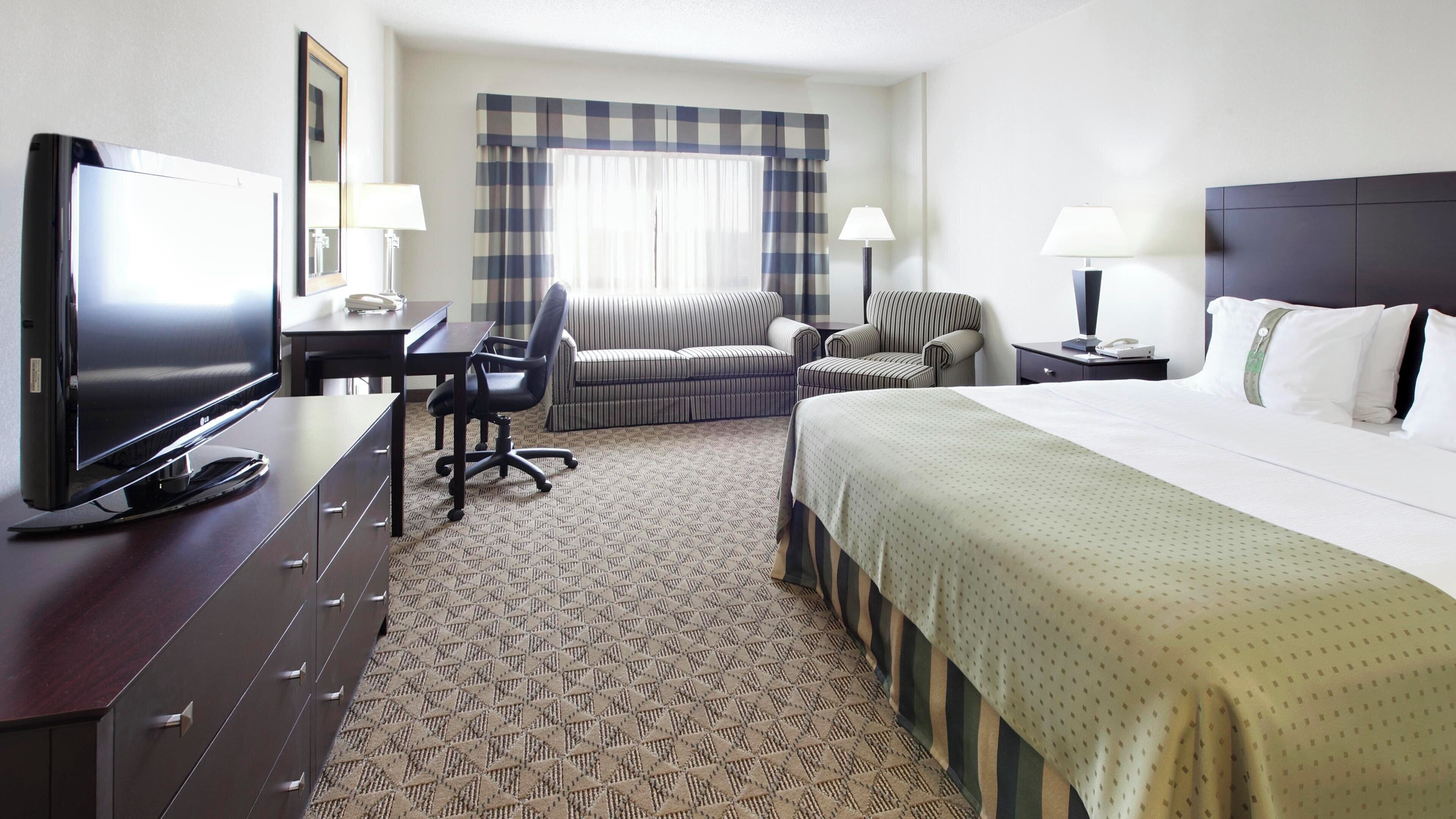 A hotel room with a bed, a desk with a television, two chairs, a sofa, and two bedside lamps.