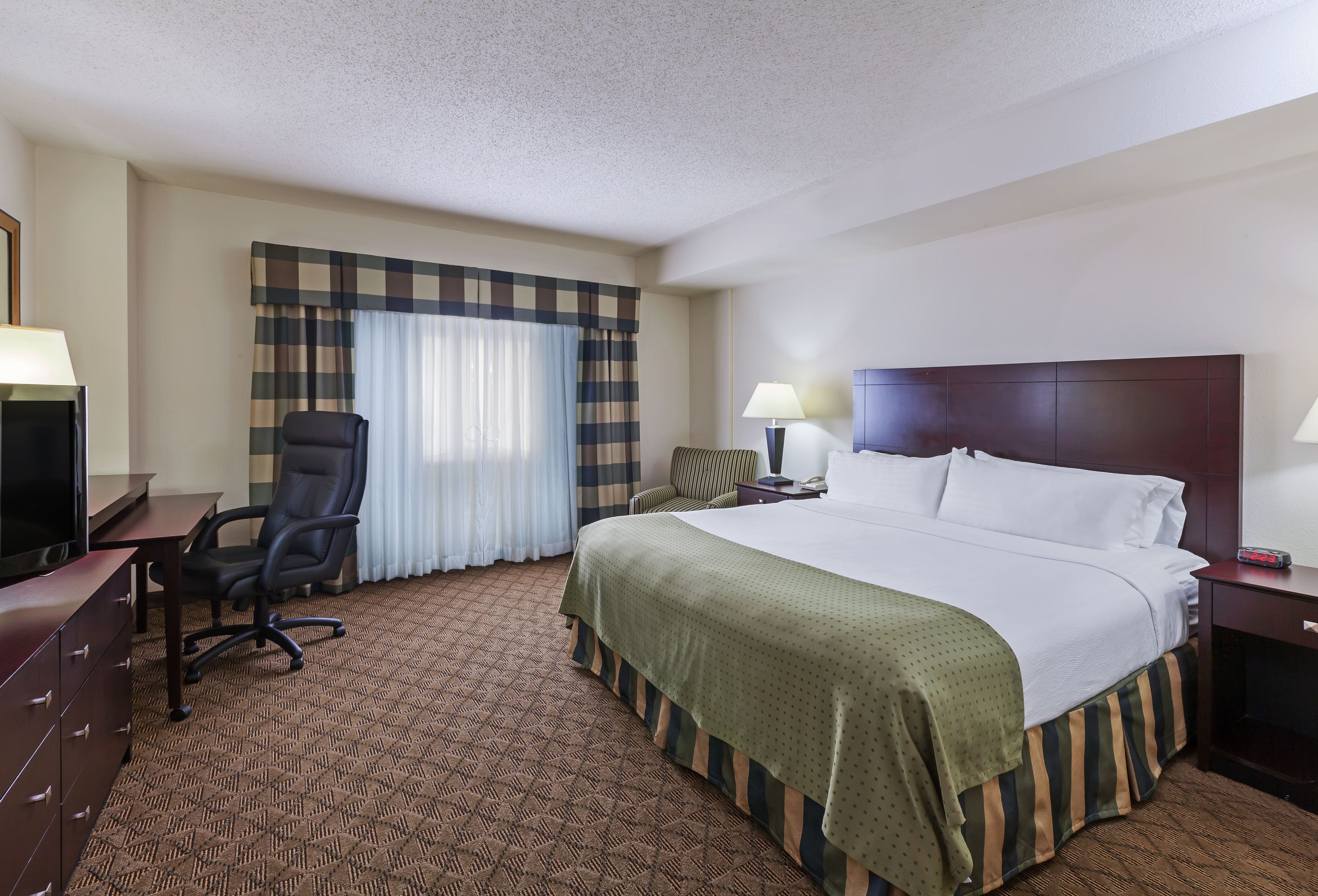 Une chambre d’hôtel avec un grand lit, un bureau avec une chaise, une télévision et une fenêtre avec des rideaux.