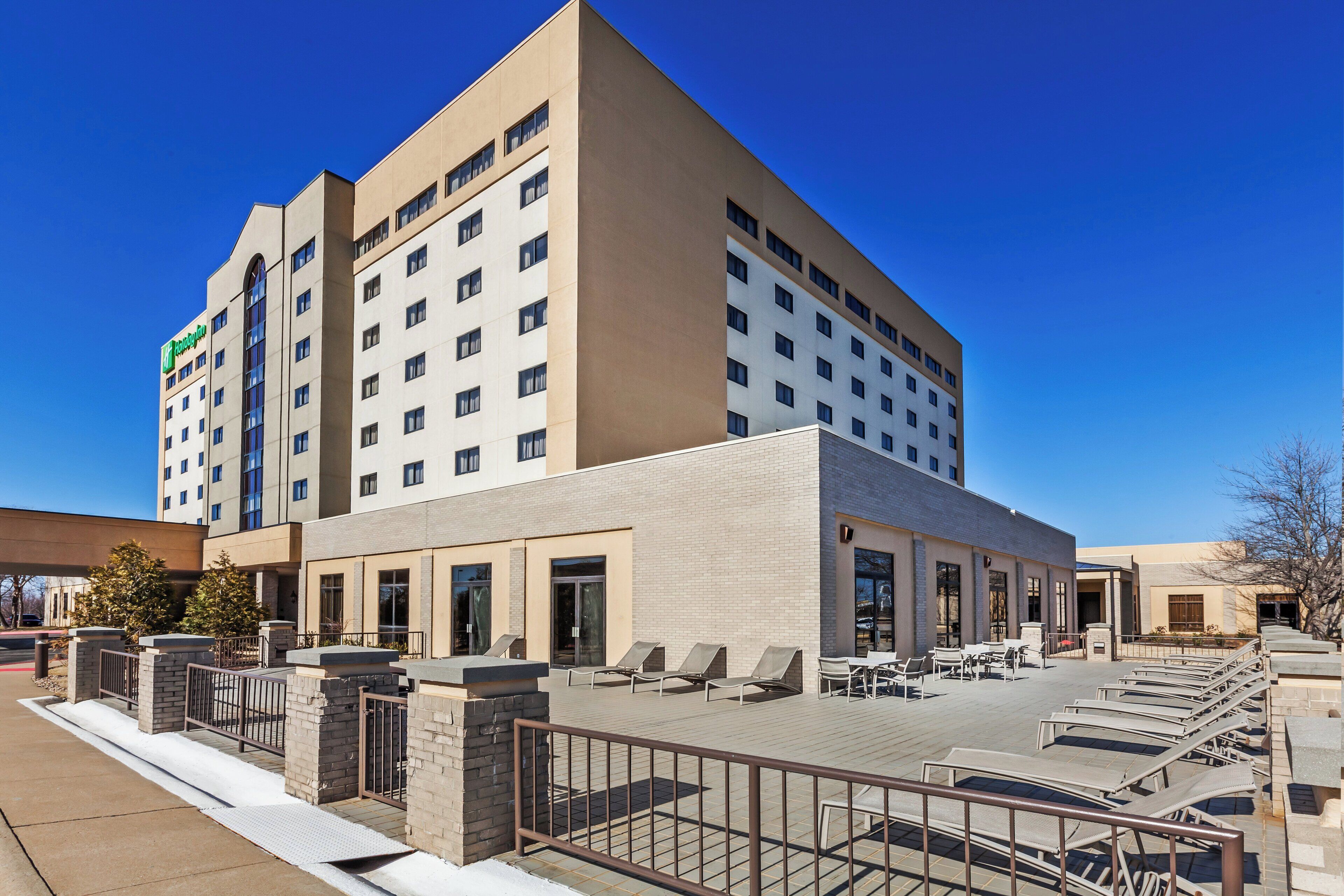 A hotel with a flat roof, multiple floors, and a patio area with outdoor seating.
