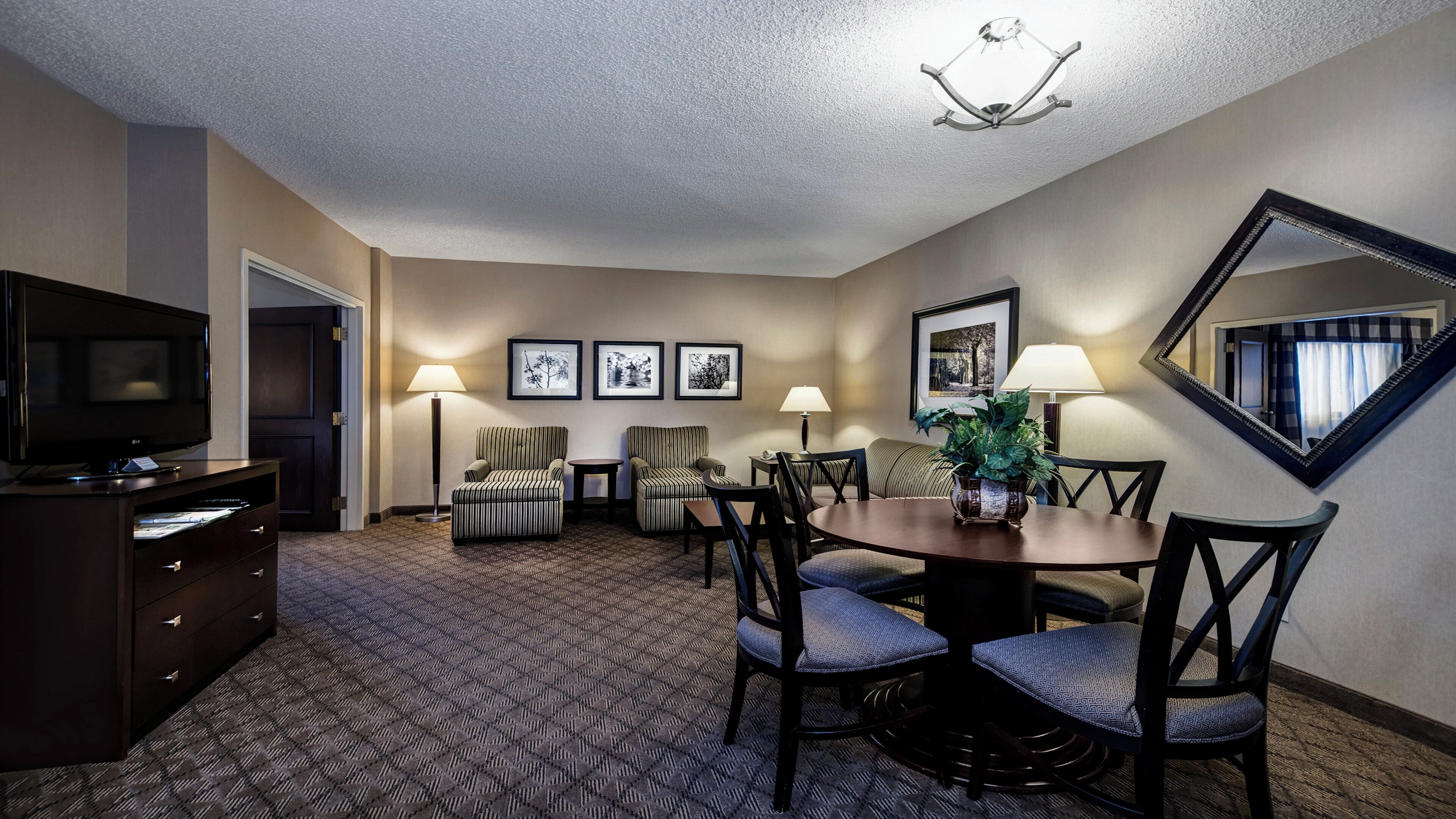 Habitación de hotel con televisor, zona de comedor con mesa y sillas, sofá y espejo en la pared.