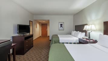 A hotel room with a television, a desk, a bed, a nightstand with a lamp, and a framed picture on the wall.