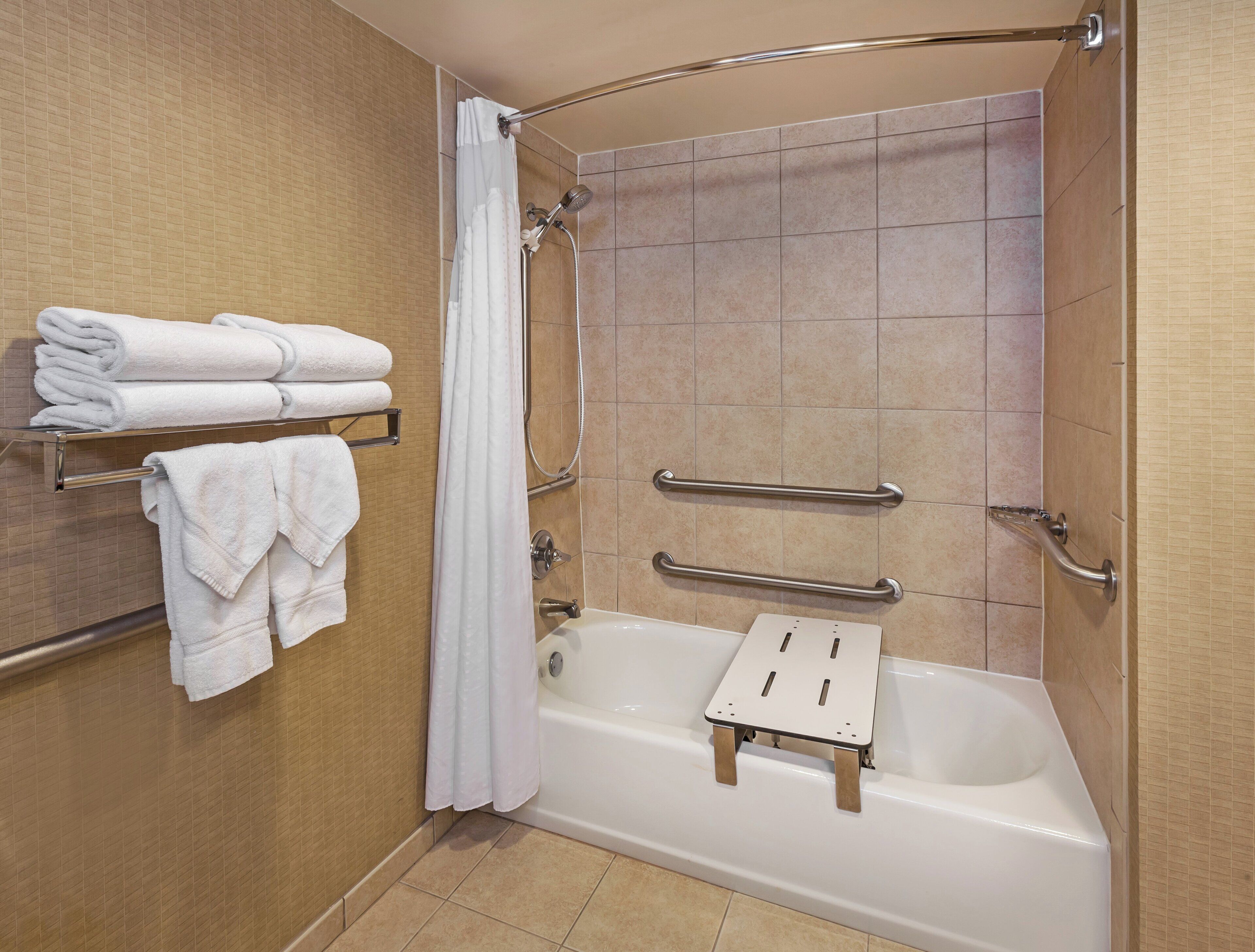 Une salle de bain avec une baignoire, une douche et une barre d’appui. Des serviettes sont posées sur un porte-serviettes.