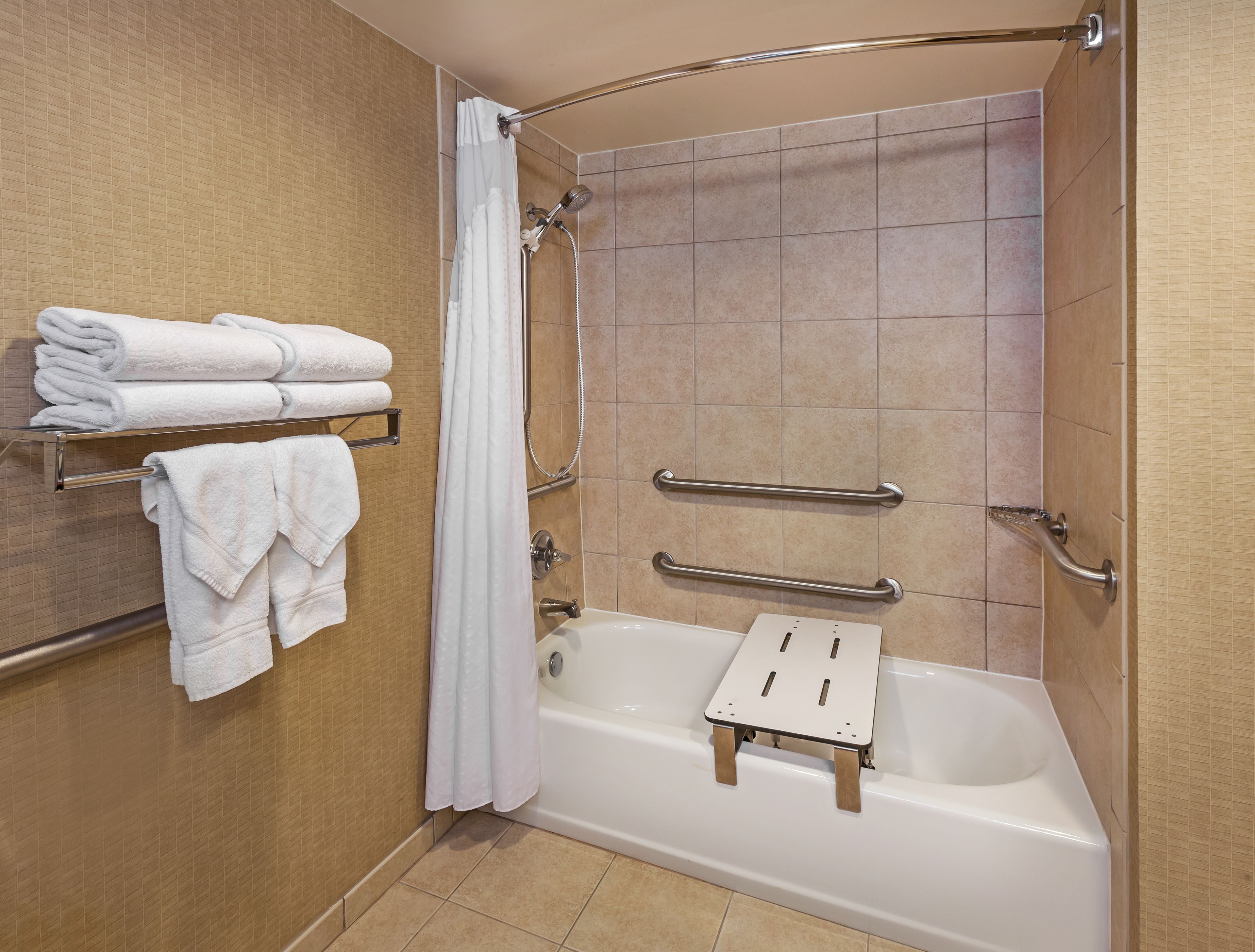 A modern bathroom with a bathtub, handrails, and a towel rack.