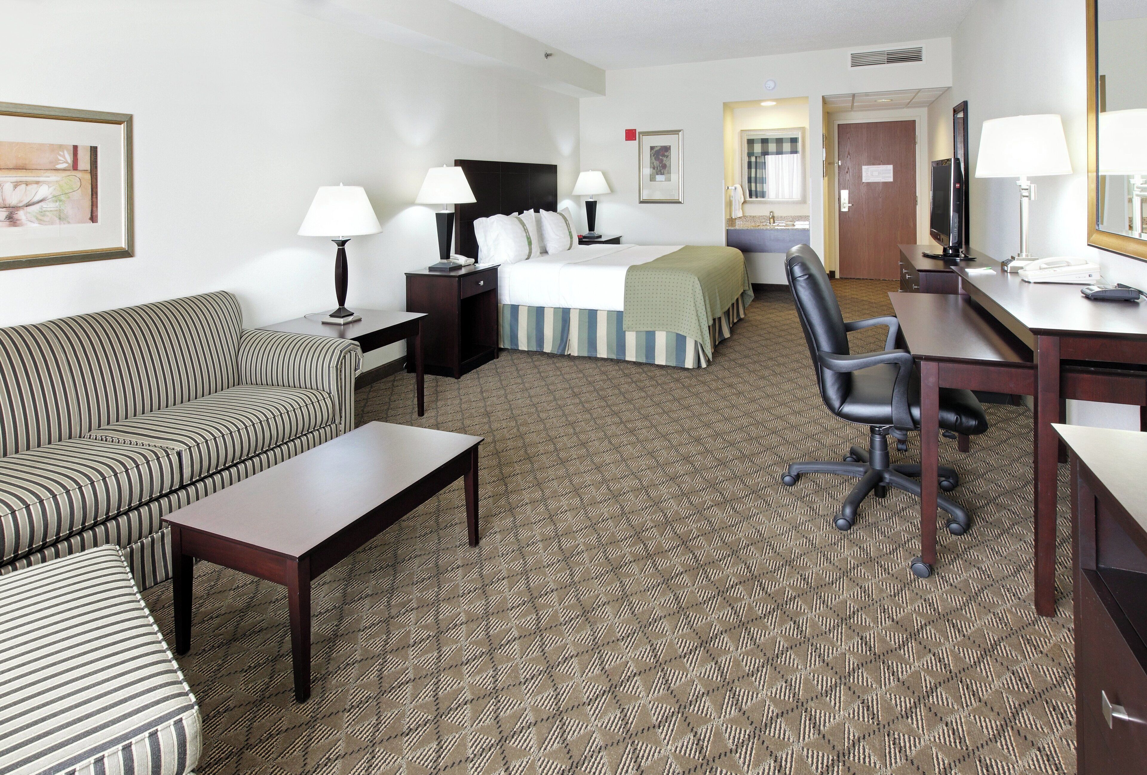 A hotel room with a bed, a desk, a chair, a sofa, and a TV.
