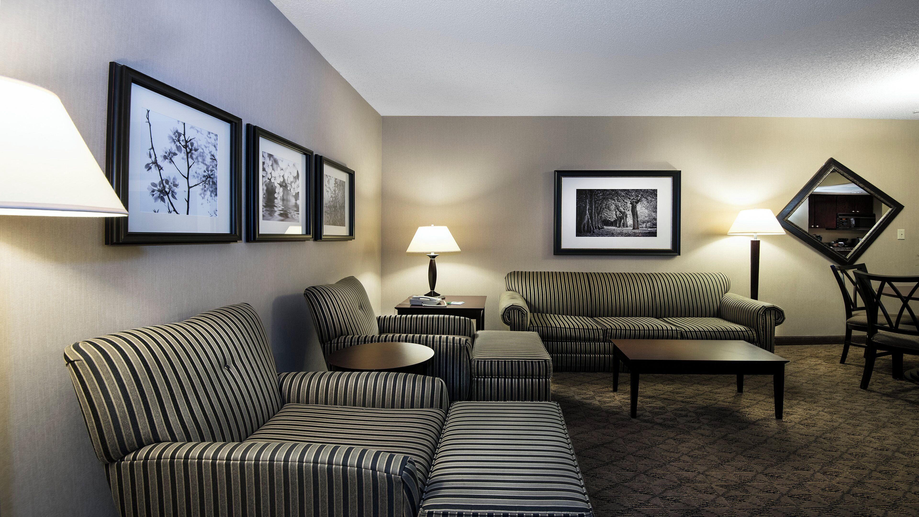 Una habitación de hotel con un sofá a rayas, un sillón a rayas, una mesita y una lámpara. Hay cuadros enmarcados en la pared.