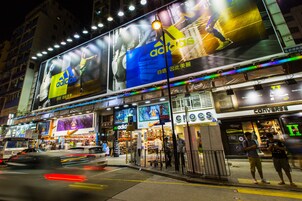 A busy urban street with large billboards, including an Adidas advertisement, and storefronts like Crocs and Converse.