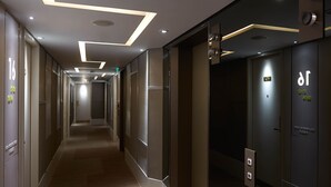 A modern hotel corridor with a long hallway, recessed lighting, and a digital elevator display. - Stanford Hotel (Kowloon)