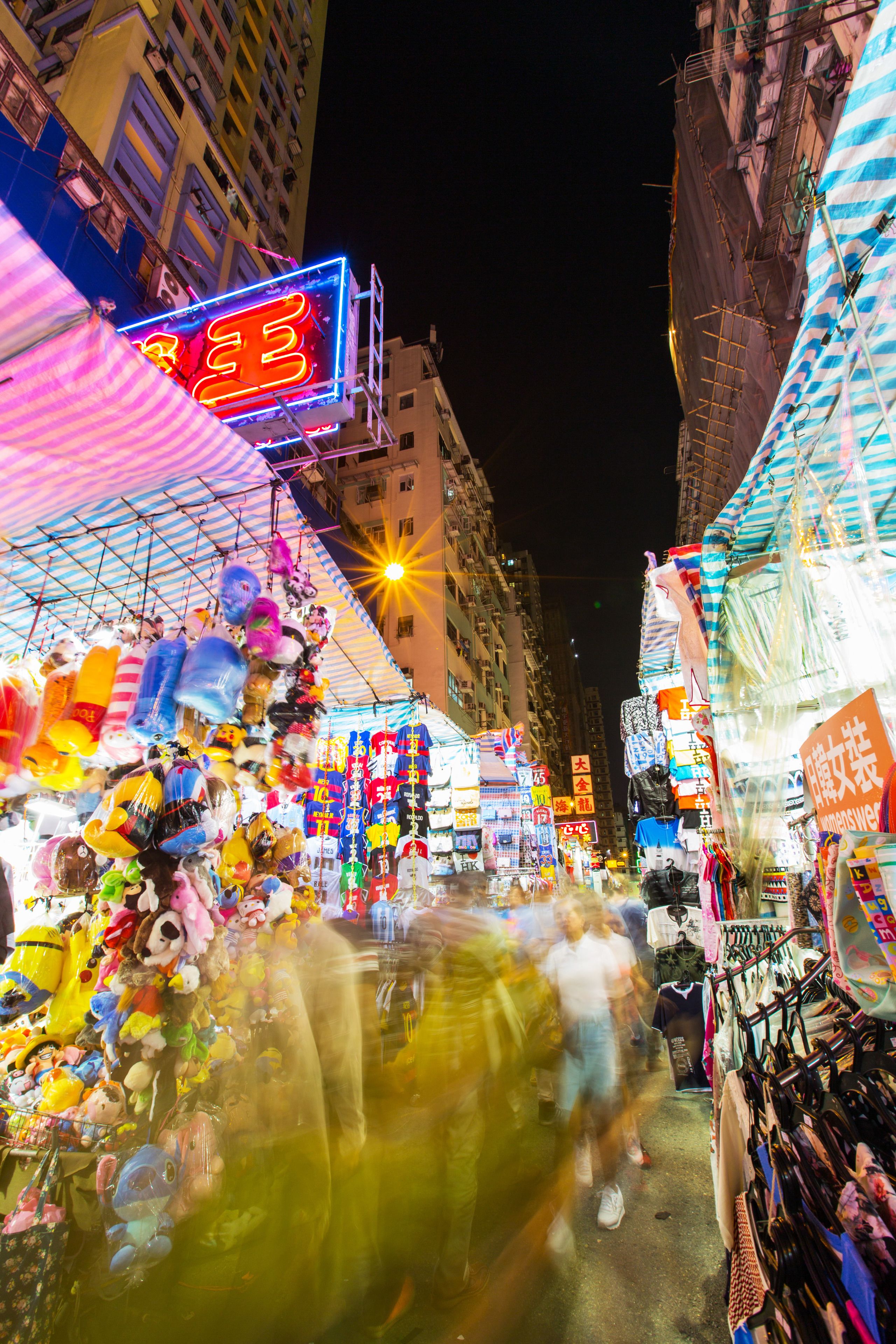 A bustling street market at night with various stalls and neon signs.