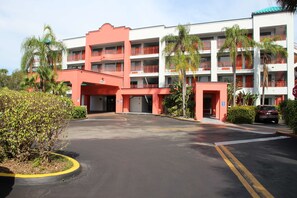 A multi-story hotel with a red and white facade, multiple balconies, and a parking area with yellow lines. - Boca Suites Deerfield Beach, SureStay Collection by BW (Deerfield Beach)