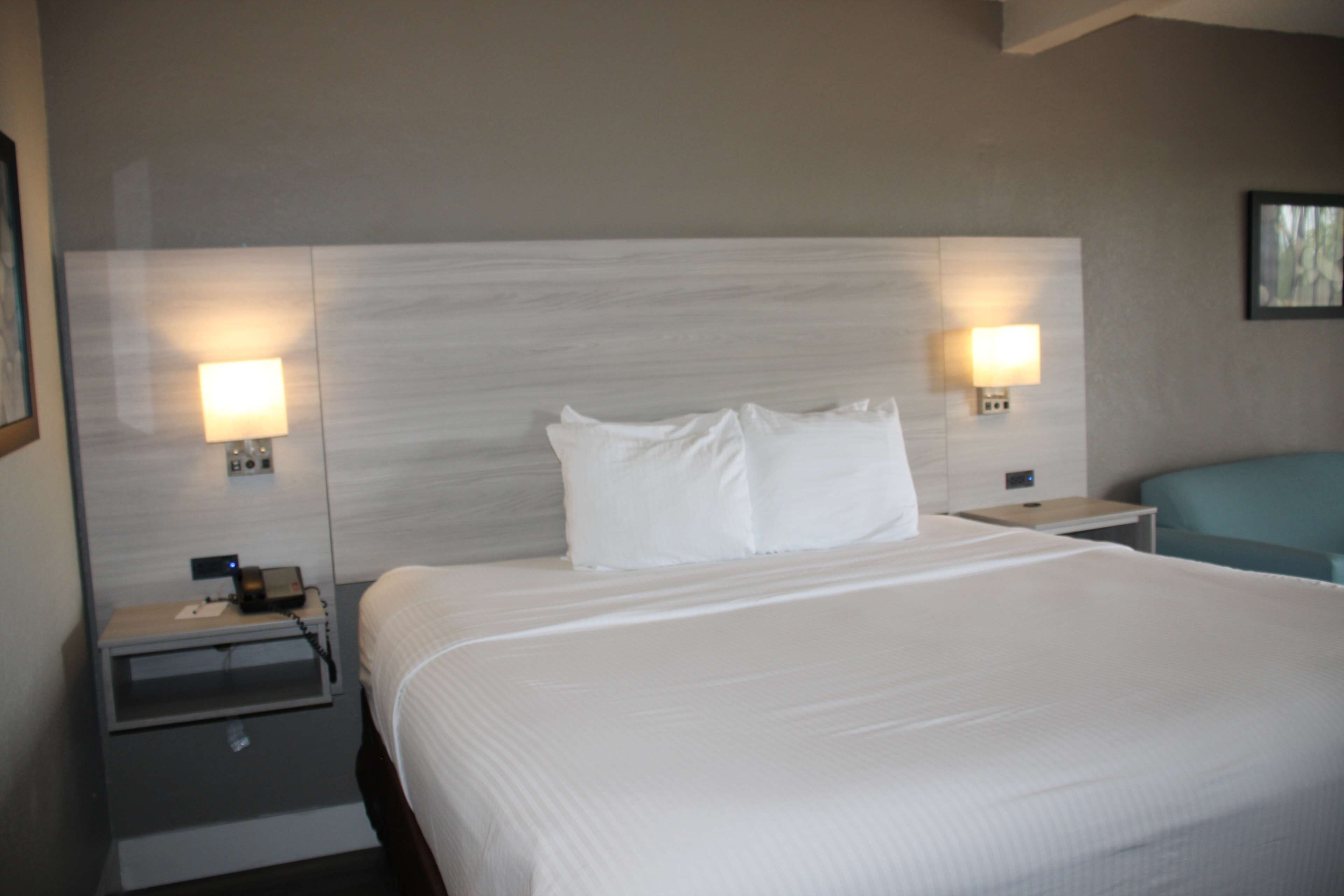 Habitación de hotel con una cama grande, dos mesitas de noche, una lámpara y una silla.